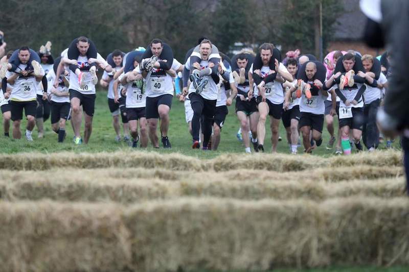 Deelnemers rennen een vrouwentillen race, een bizarre hardloopwedstrijd en romantische uitdaging met humor.